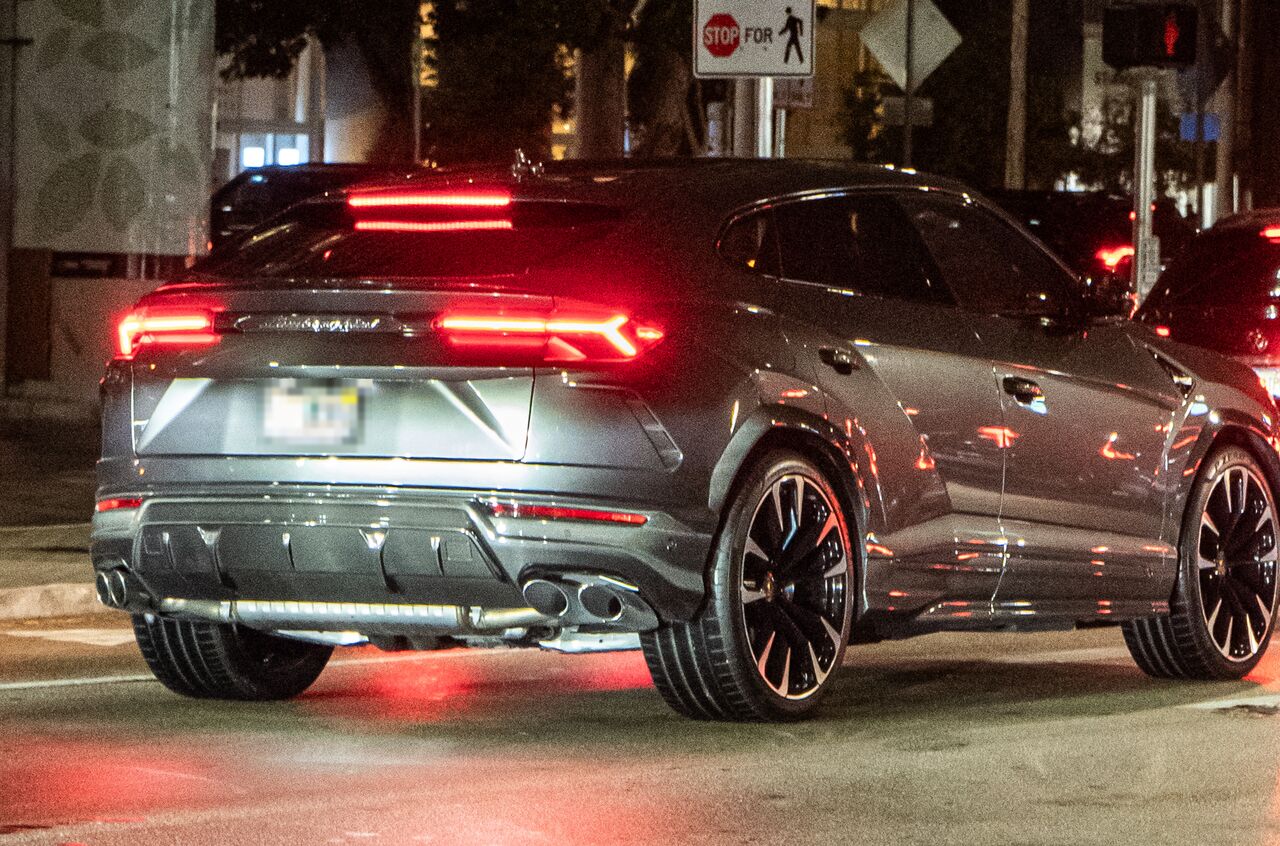 Traseira de um Lamborghini Urus cinza à noite, com as lanternas acesas e a tampa do porta-malas fechada